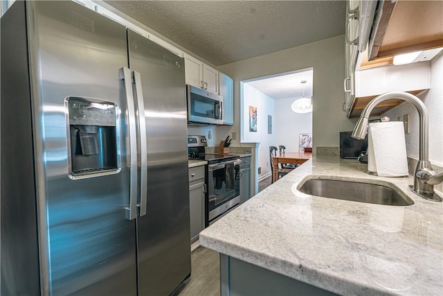 kitchen with a textured ceiling, dark hardwood / wood-style flooring, stainless steel appliances, sink, and light stone counters