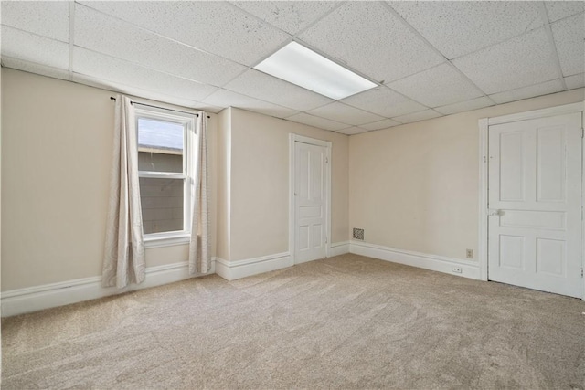 spare room featuring a paneled ceiling and light colored carpet