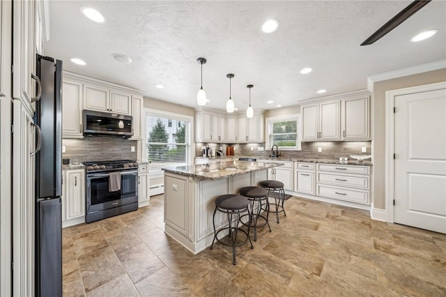 kitchen with a center island, appliances with stainless steel finishes, light stone countertops, white cabinetry, and hanging light fixtures