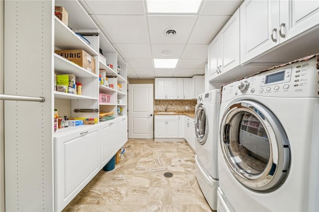 clothes washing area with cabinets, sink, and washer and clothes dryer