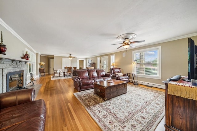 living room with baseboard heating, ceiling fan, hardwood / wood-style flooring, a stone fireplace, and ornamental molding