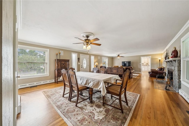 dining space with baseboard heating, ceiling fan, a fireplace, hardwood / wood-style floors, and ornamental molding