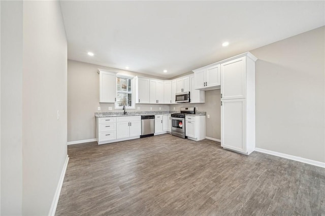 kitchen with wood-type flooring, appliances with stainless steel finishes, sink, white cabinetry, and light stone countertops