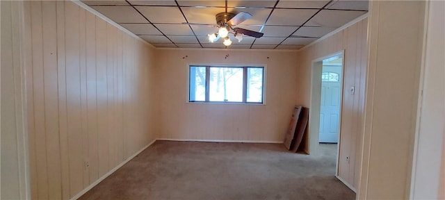 empty room featuring ceiling fan, wood walls, a paneled ceiling, and light carpet