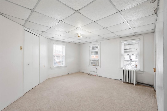 unfurnished bedroom with light carpet, radiator heating unit, multiple windows, and a paneled ceiling