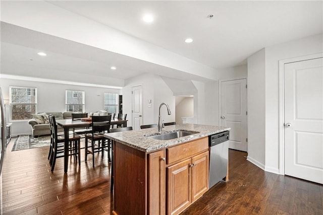 kitchen with dishwasher, a kitchen island with sink, sink, dark wood-type flooring, and light stone counters