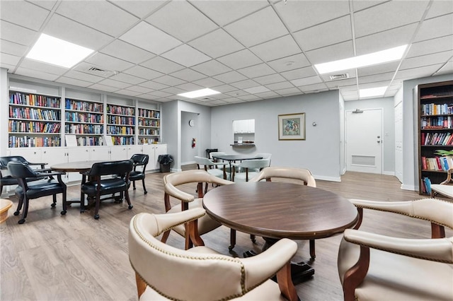 dining area featuring a drop ceiling, built in features, and light hardwood / wood-style flooring