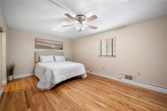 bedroom featuring ceiling fan, light hardwood / wood-style floors, and a skylight