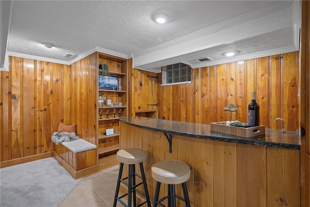 bar featuring a textured ceiling, wooden walls, dark stone countertops, ornamental molding, and light tile patterned flooring