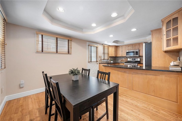 dining area featuring sink, a raised ceiling, crown molding, and light hardwood / wood-style floors