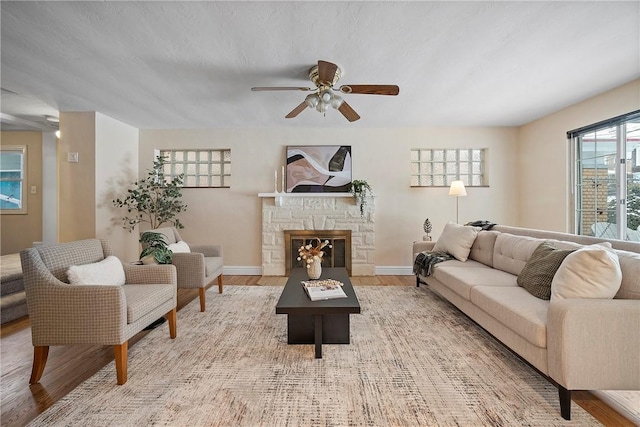 living room with light wood-type flooring, ceiling fan, a textured ceiling, and a fireplace