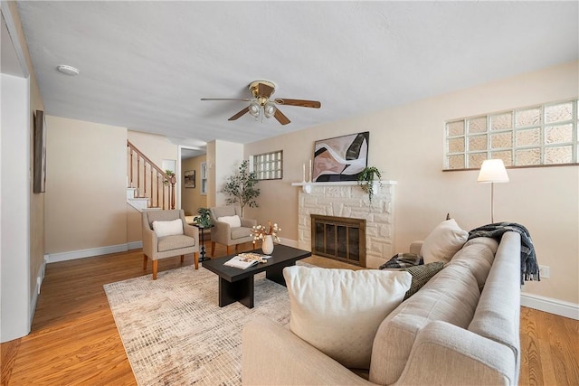 living room featuring hardwood / wood-style flooring, ceiling fan, and a stone fireplace