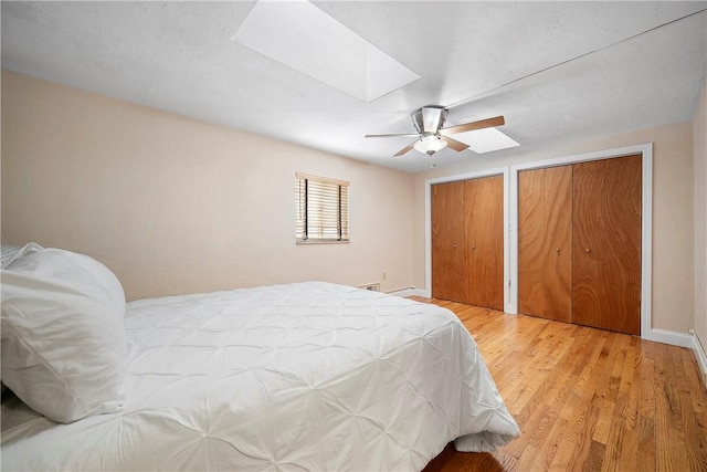 bedroom featuring ceiling fan, two closets, hardwood / wood-style flooring, and a skylight