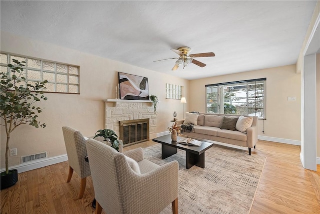 living room featuring ceiling fan, light wood-type flooring, and a stone fireplace