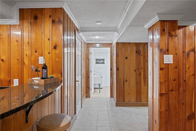 hallway with wood walls, a textured ceiling, light tile patterned floors, and ornamental molding