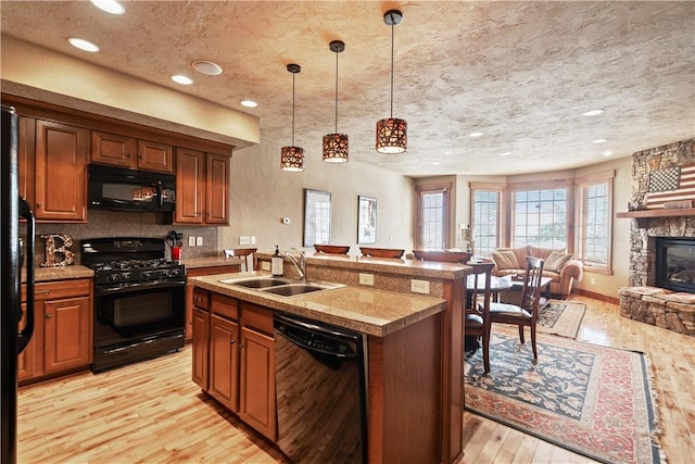 kitchen featuring hanging light fixtures, sink, light wood-type flooring, a kitchen island with sink, and black appliances