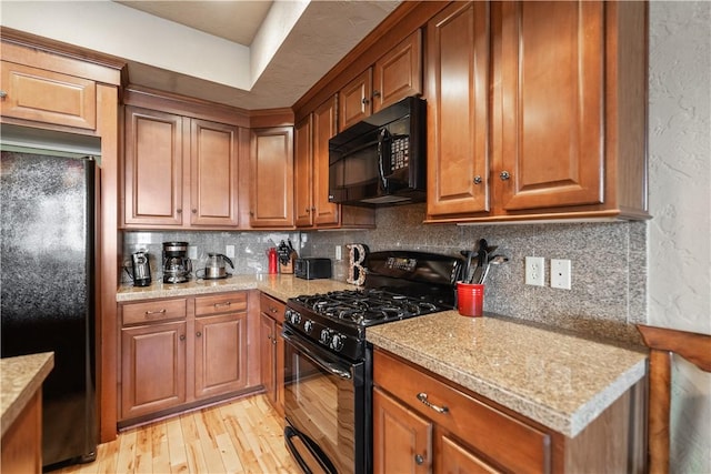 kitchen featuring black appliances, light stone counters, light hardwood / wood-style flooring, and tasteful backsplash