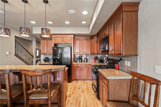 kitchen with light stone countertops, black appliances, tasteful backsplash, hanging light fixtures, and a breakfast bar area