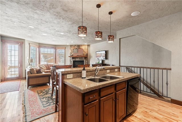 kitchen featuring dishwasher, decorative light fixtures, light hardwood / wood-style floors, sink, and a kitchen island with sink