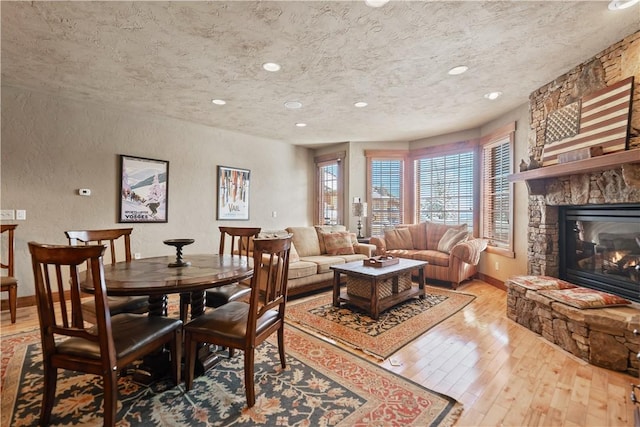 dining space with a textured ceiling, light hardwood / wood-style flooring, and a stone fireplace