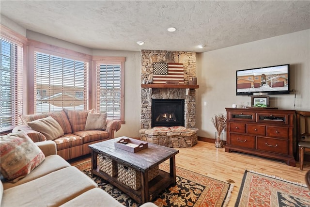 living room with hardwood / wood-style flooring, a textured ceiling, and a stone fireplace