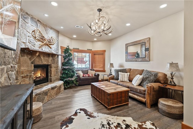 living room featuring hardwood / wood-style flooring, a stone fireplace, and an inviting chandelier