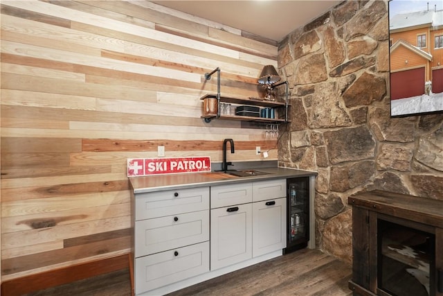 kitchen with sink, wood walls, dark wood-type flooring, and beverage cooler