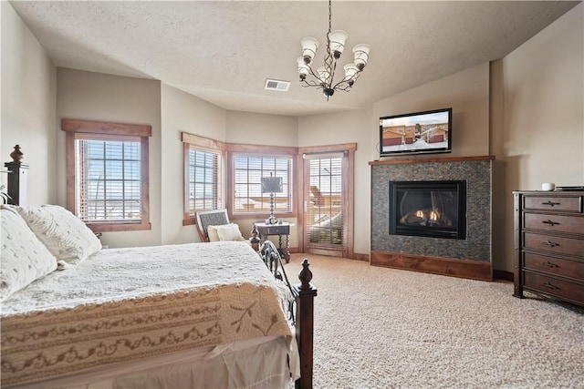 bedroom featuring a tile fireplace, an inviting chandelier, a textured ceiling, and carpet floors