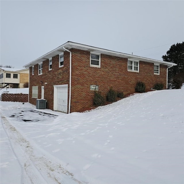 snow covered property with central AC unit and a garage