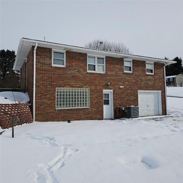 snow covered property with central AC and a garage