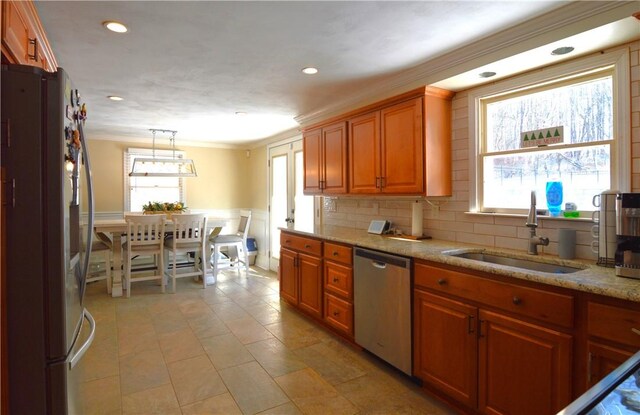 kitchen with appliances with stainless steel finishes, sink, hanging light fixtures, light stone counters, and crown molding