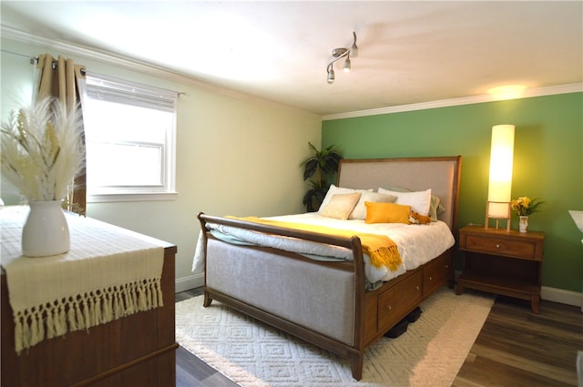 bedroom with dark wood-type flooring, track lighting, and ornamental molding