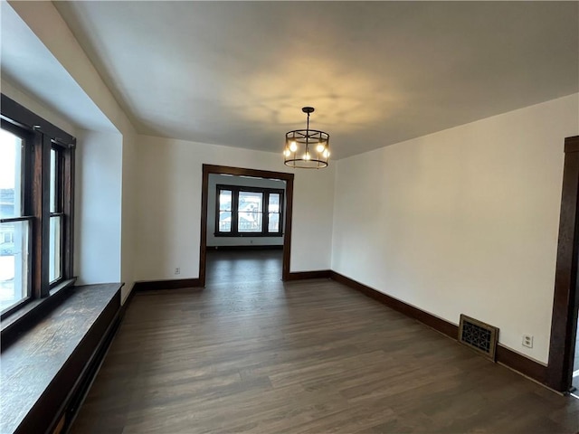 spare room with plenty of natural light, a chandelier, and dark hardwood / wood-style flooring