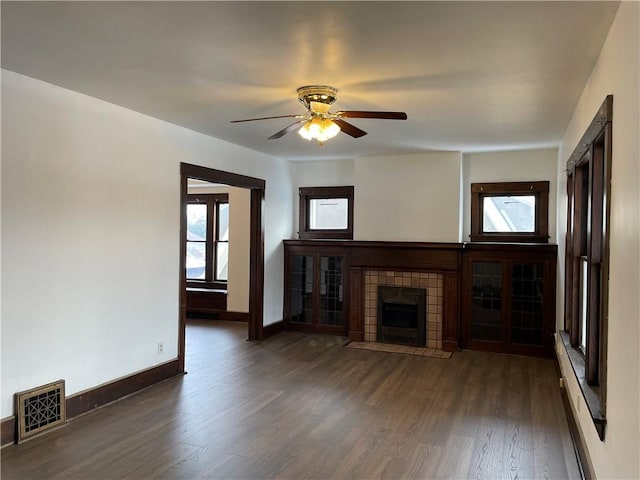 unfurnished living room with ceiling fan, a tile fireplace, and dark wood-type flooring