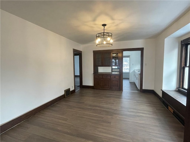 unfurnished dining area with an inviting chandelier and dark hardwood / wood-style flooring