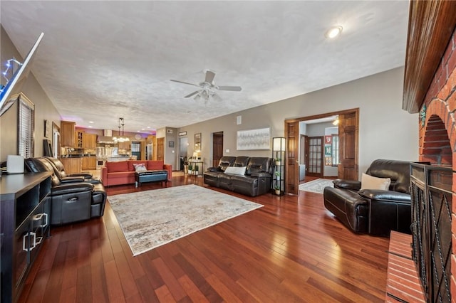 living room with ceiling fan with notable chandelier, dark wood-type flooring, and a textured ceiling