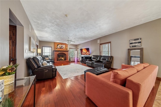 living room with ceiling fan, hardwood / wood-style flooring, a textured ceiling, and a brick fireplace