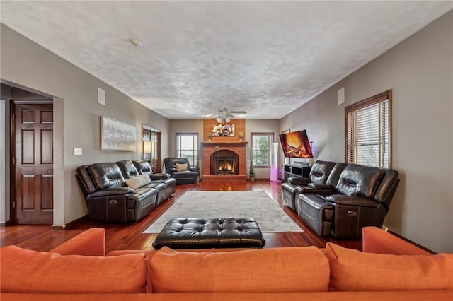 living room featuring a brick fireplace, wood-type flooring, a textured ceiling, and ceiling fan