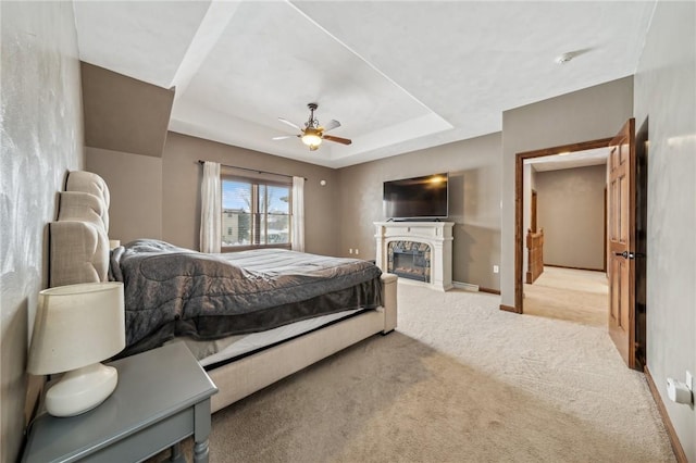 bedroom featuring ceiling fan, a tray ceiling, and light carpet