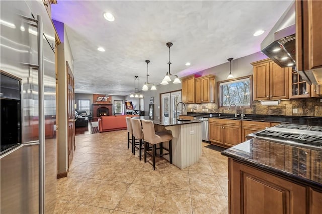 kitchen featuring appliances with stainless steel finishes, a kitchen breakfast bar, decorative light fixtures, backsplash, and an island with sink