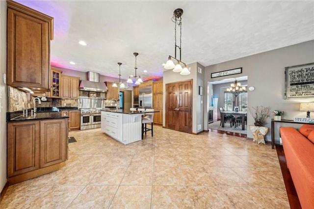 kitchen with pendant lighting, wall chimney exhaust hood, double oven range, backsplash, and a kitchen island with sink