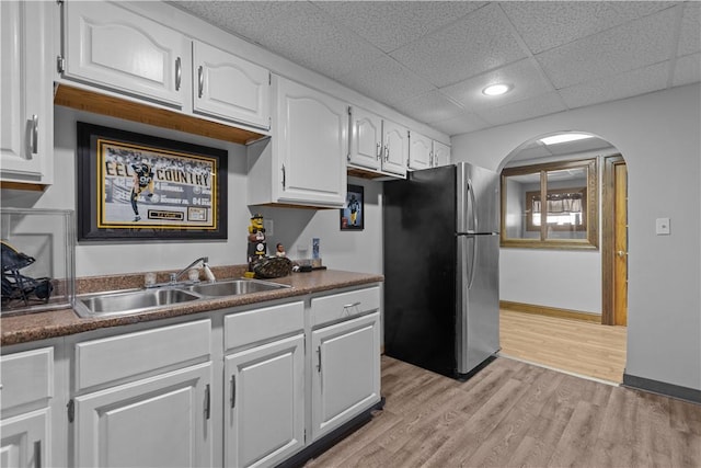 kitchen with sink, white cabinetry, a paneled ceiling, light wood-type flooring, and stainless steel refrigerator