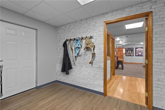 foyer entrance featuring wood-type flooring, a paneled ceiling, and brick wall