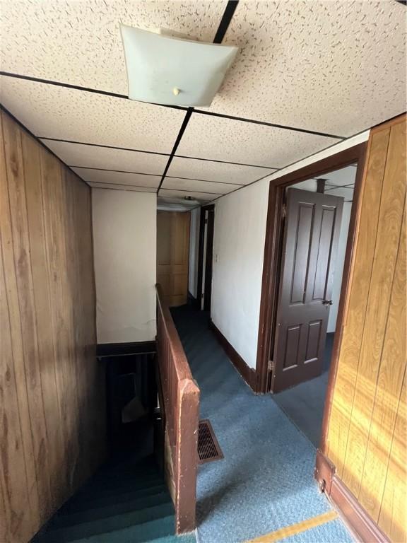 staircase featuring carpet, a paneled ceiling, and wooden walls