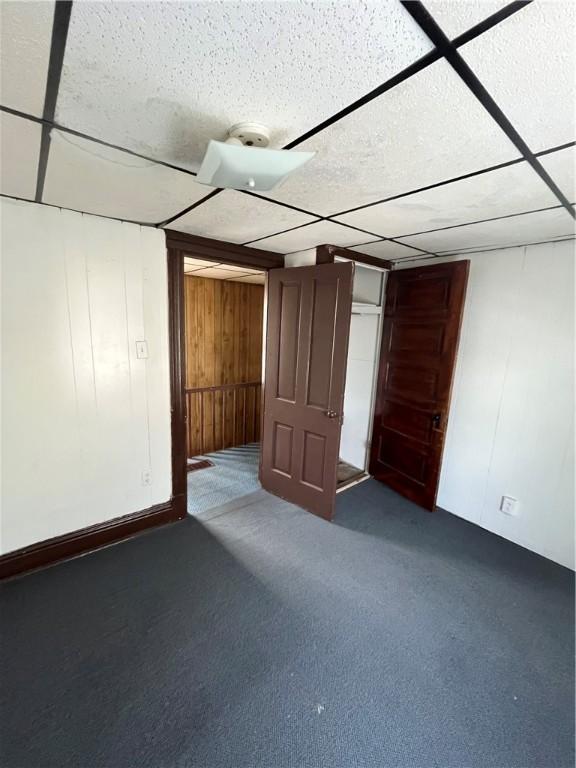 basement with dark carpet, a drop ceiling, and wood walls