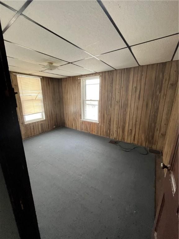 empty room featuring a drop ceiling and wood walls