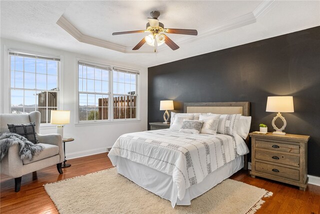 bedroom with ceiling fan, hardwood / wood-style floors, crown molding, and a raised ceiling