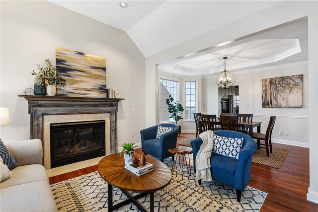 living room featuring wood-type flooring, a premium fireplace, a raised ceiling, and a chandelier