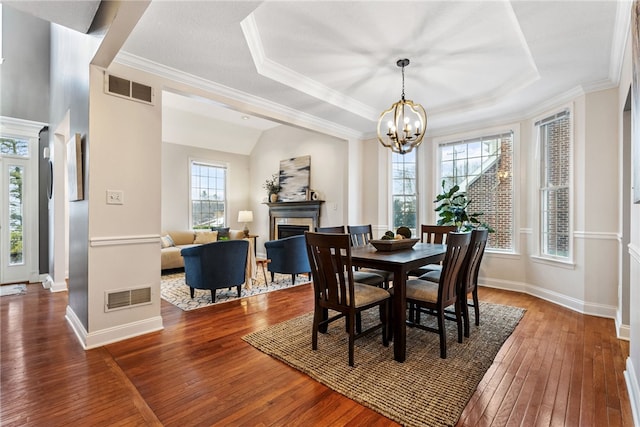 dining room featuring an inviting chandelier, ornamental molding, dark hardwood / wood-style floors, and a raised ceiling