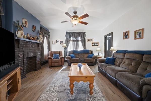 living room featuring ceiling fan, hardwood / wood-style floors, and a brick fireplace